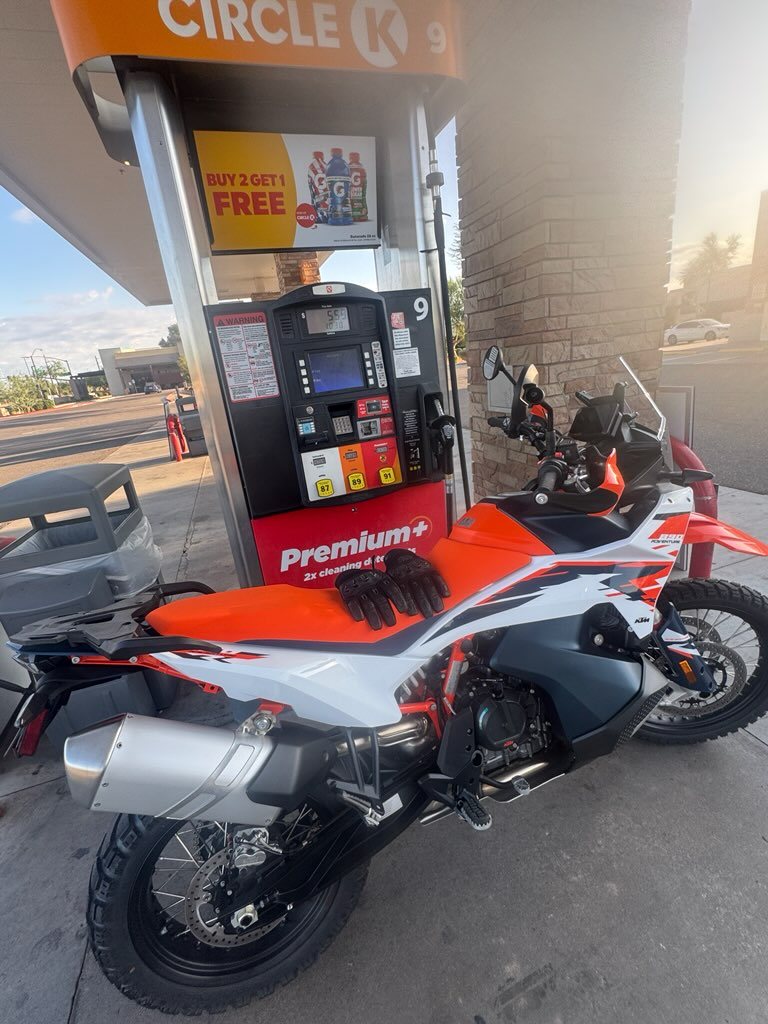 KTM 890 Adventure at a fuel stop with a soft bag strapped to the rear and gloves left on the seat